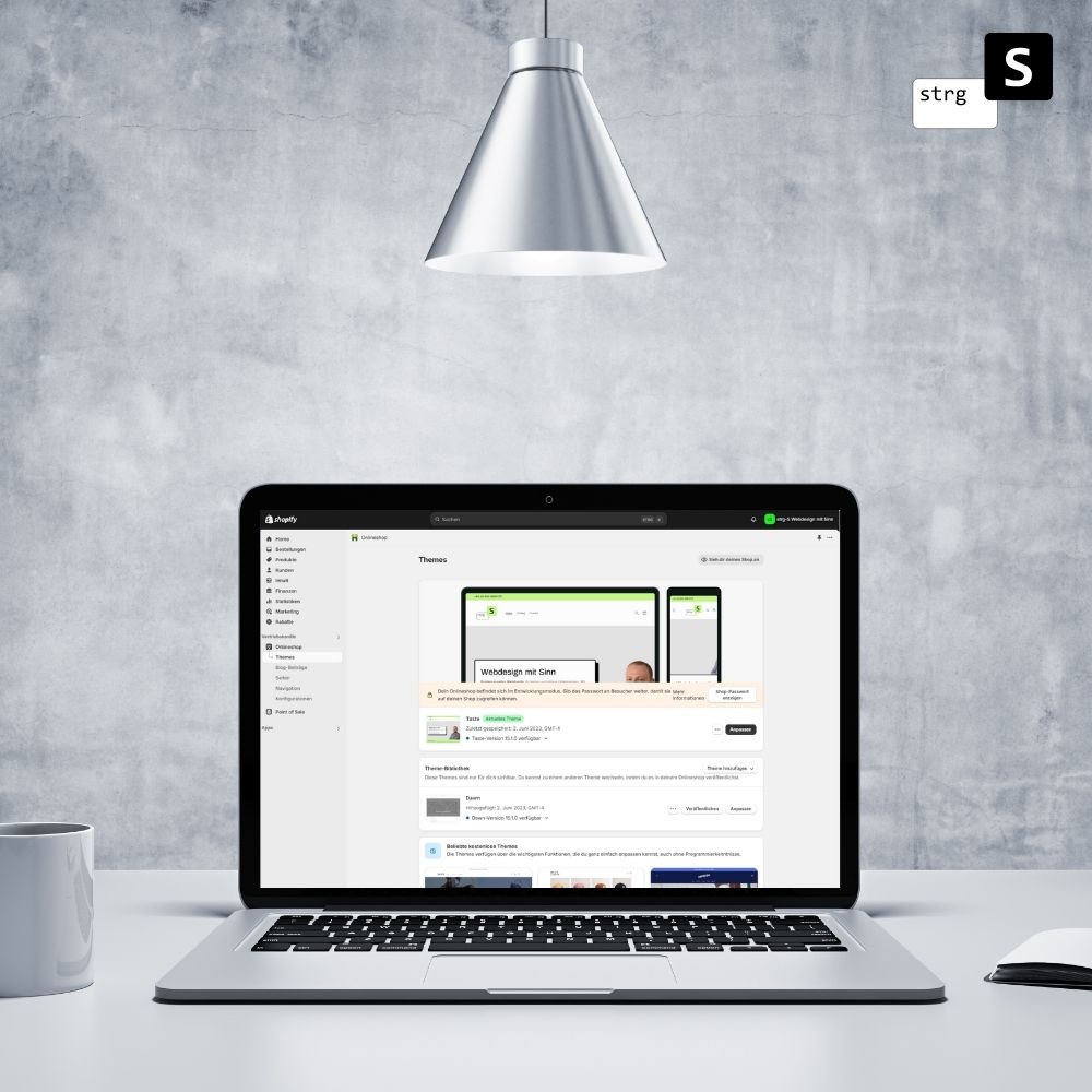 Ein Laptop auf einem Schreibtisch, auf dem eine Webseite mit der Anzeige *Hilfe bei Shopify* angezeigt wird. In der Nähe stehen vor einem grauen Hintergrund eine Tasse und eine Lampe.